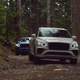 A pair of Bentley Bentaygas on a forest road.